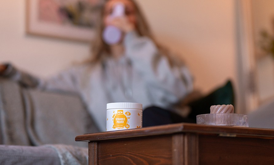 Healthwell C-vitamin pulver står på et bord med en kvinde i baggrunden. Healthwell C-vitamin pulver står på et bord med en kvinde i baggrunden.